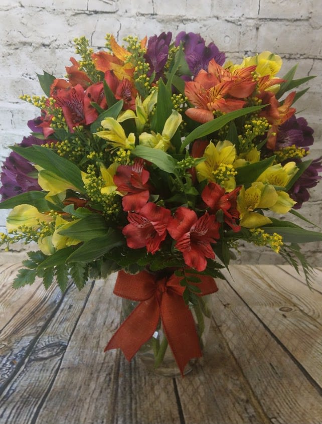 Mixed bouquet of red, yellow, orange, and purple flowers in a glass vase