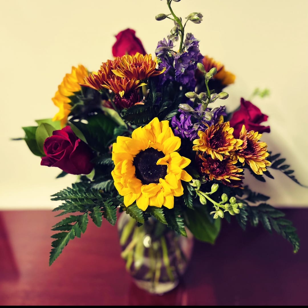 Bouquet of sunflowers, purple flowers, and red roses in a glass vase