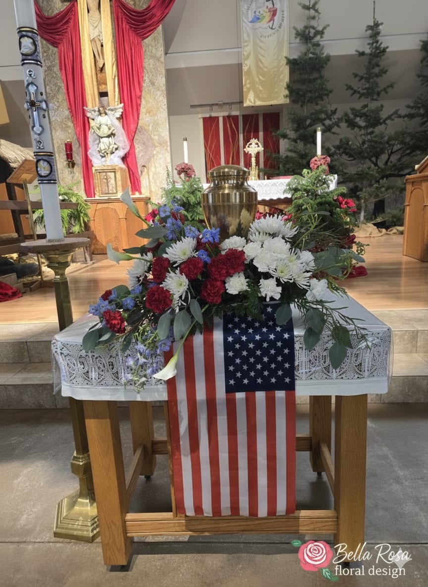 Floral arrangement with red, white, and blue flowers on a table draped with an American flag.