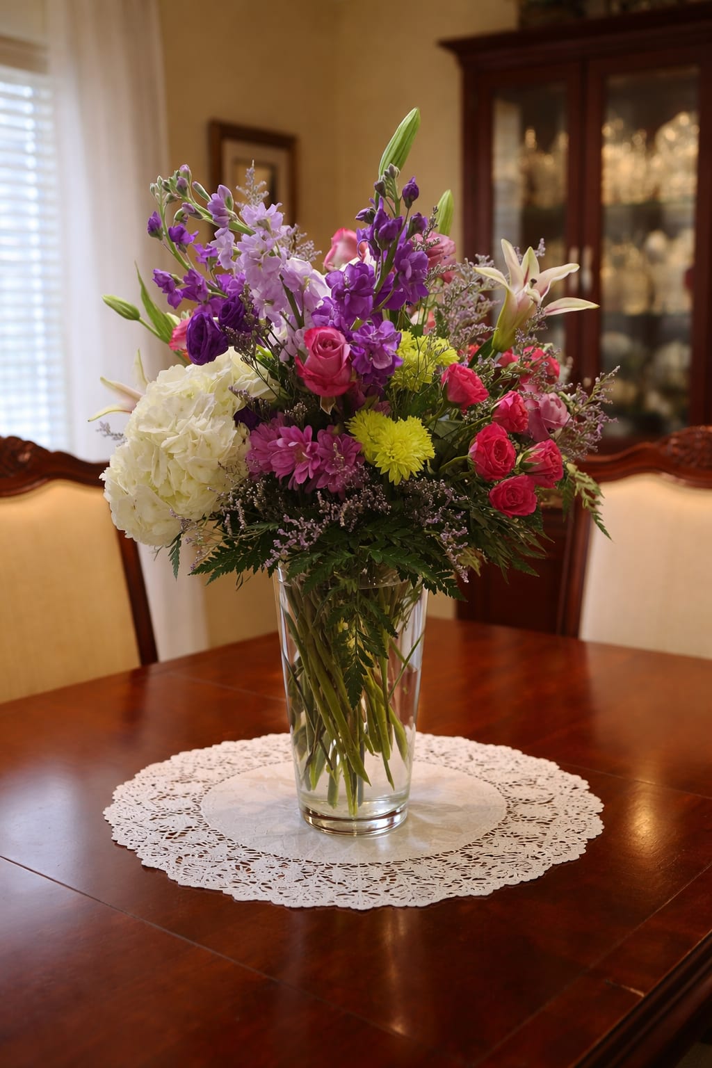 Mixed bouquet of purple, pink, white, and yellow flowers in a clear glass vase