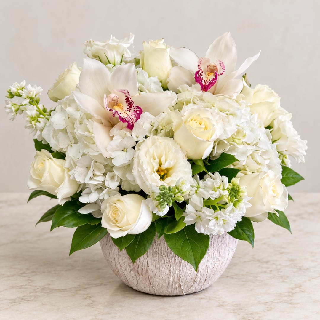 White floral arrangement in a round vase with roses, hydrangeas, and orchids
