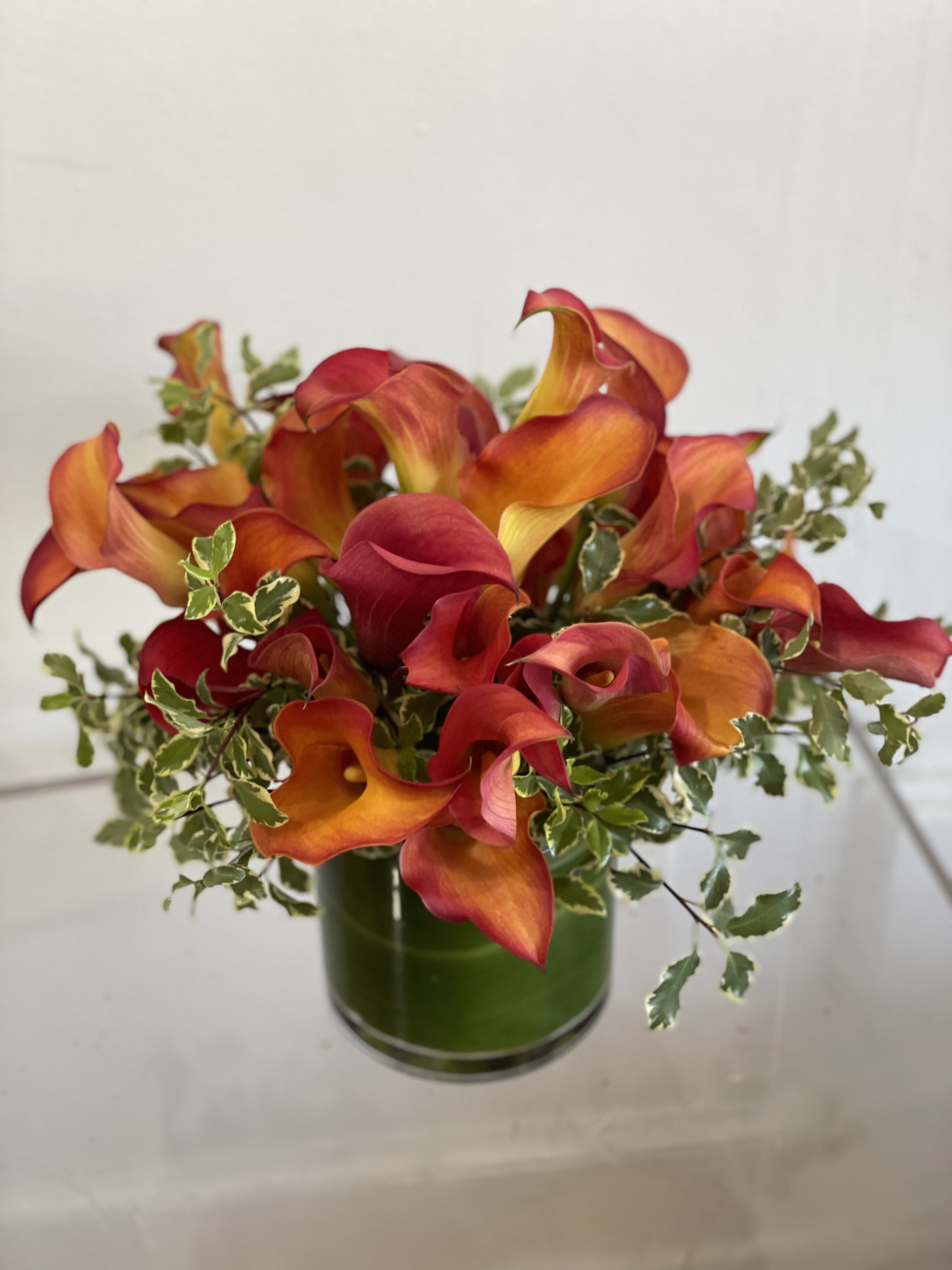 Orange and red calla lilies arranged in a green glass vase