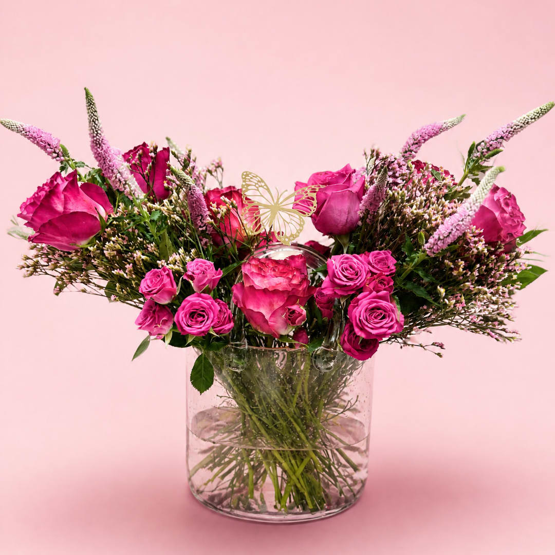 Pink roses and spray roses in a clear glass vase with a butterfly pick