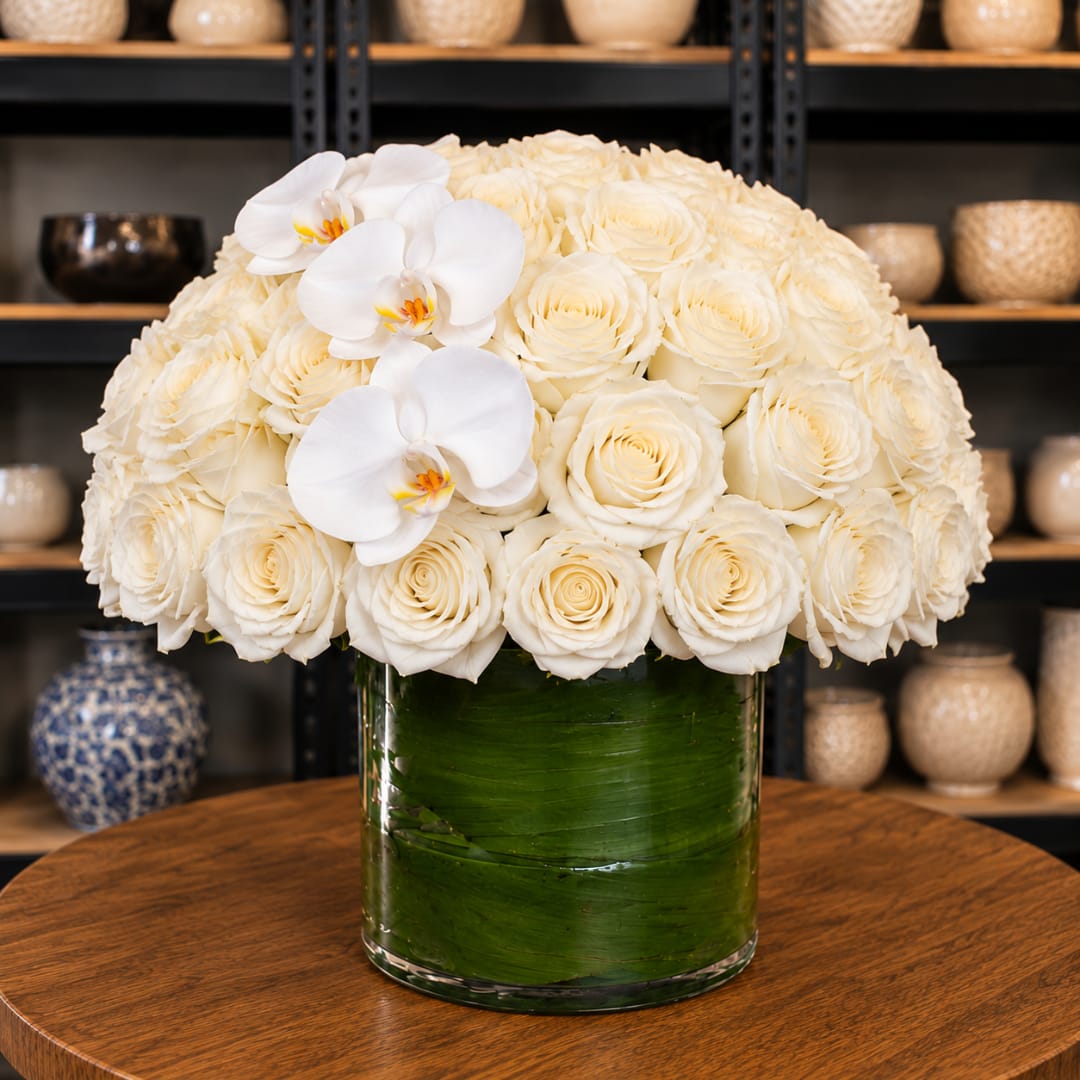 White rose arrangement with three white orchids in a glass vase