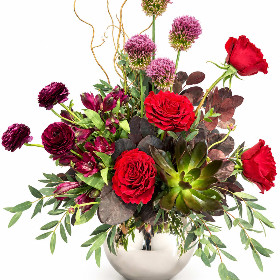 Red roses and purple blooms arranged in a silver vase