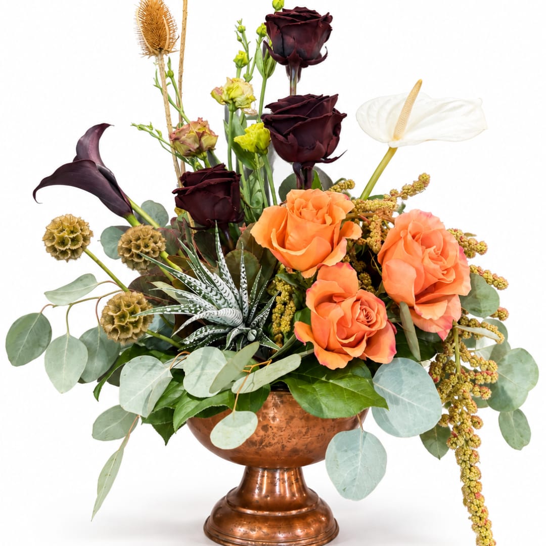 Mixed floral arrangement in a copper vase with orange and dark burgundy blooms
