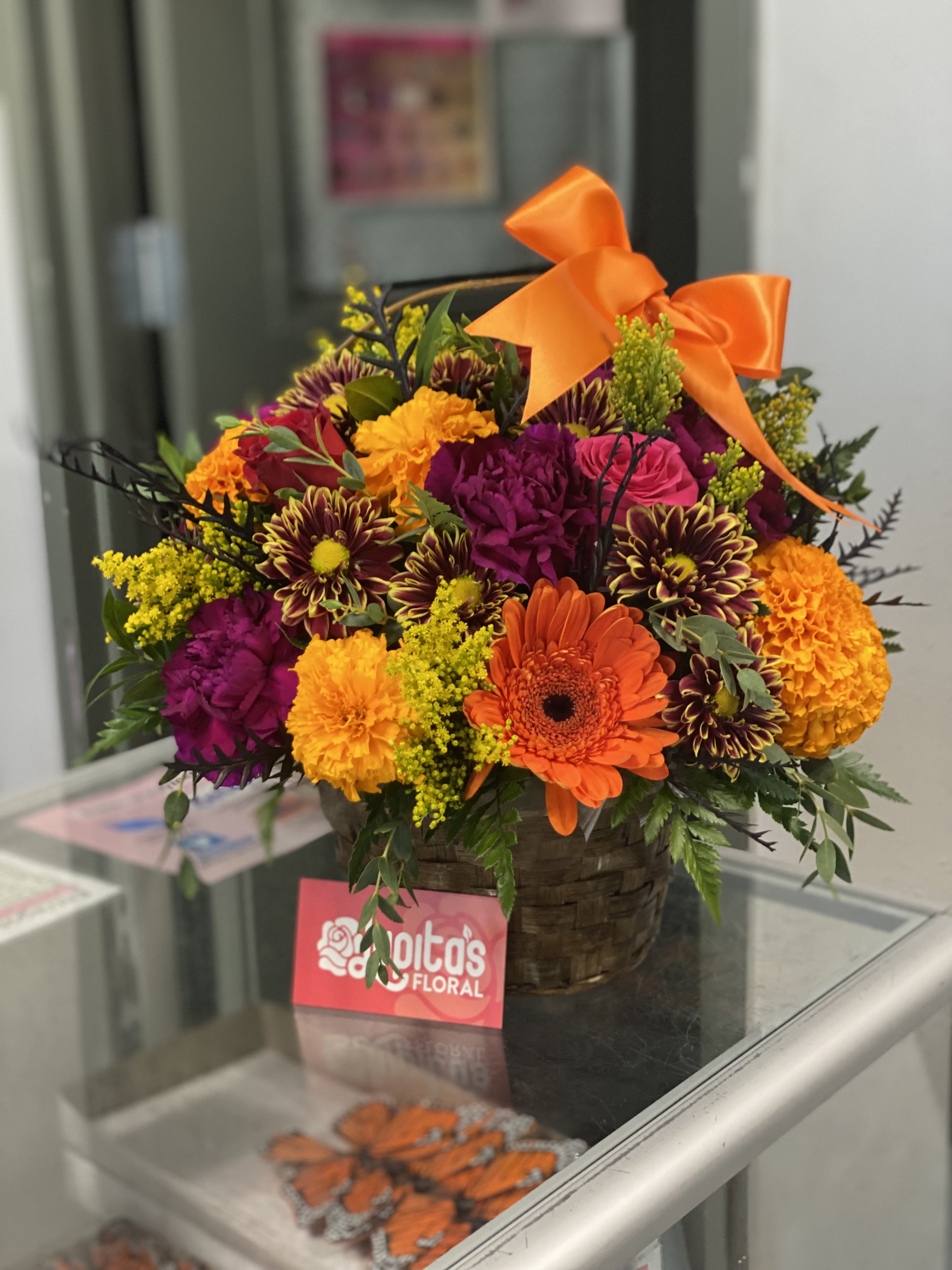 Colorful mixed flower arrangement in a basket with an orange bow