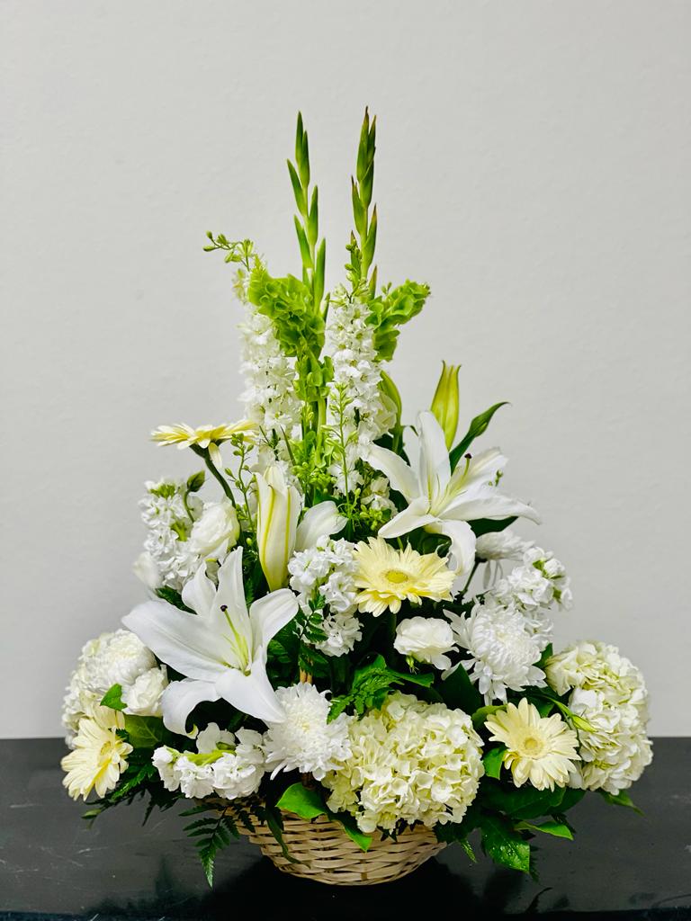 White lilies and pale yellow daisies in a wicker basket arrangement