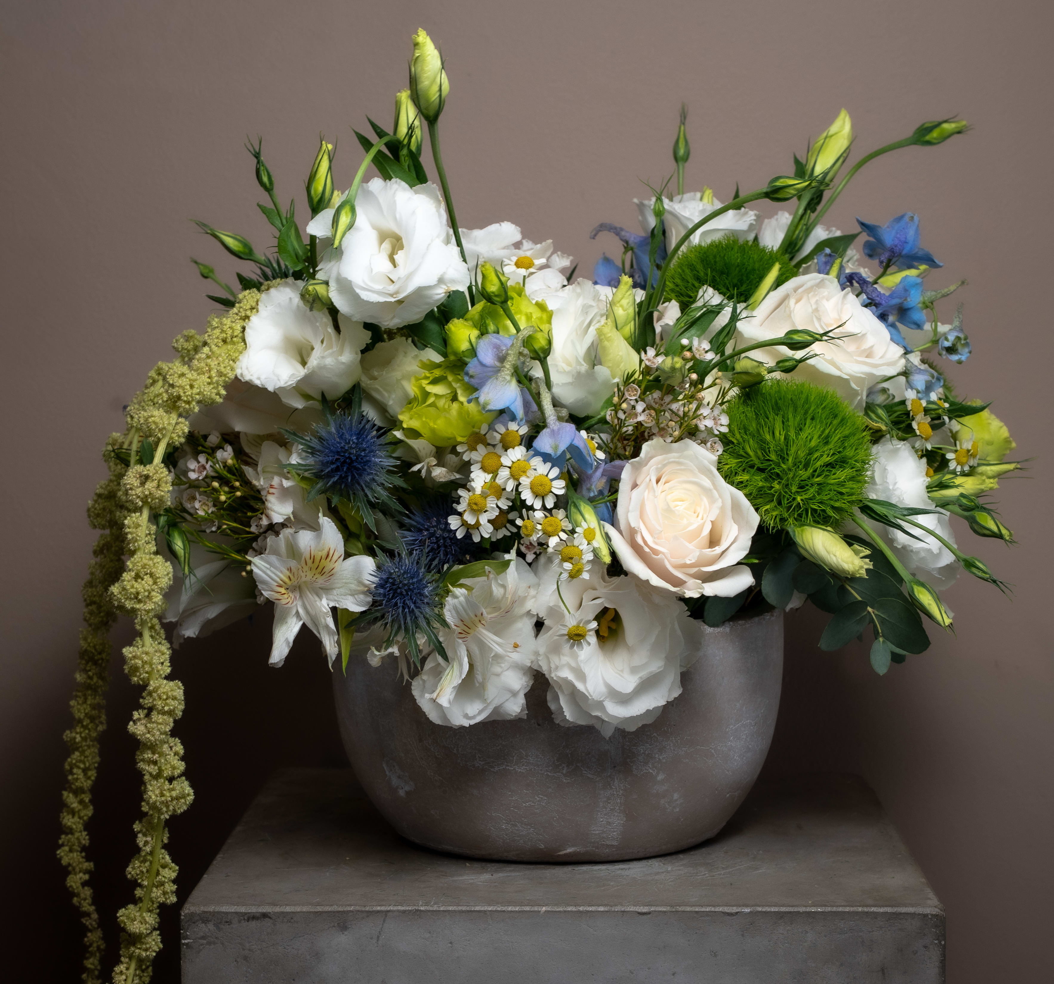 Mixed bouquet of white, blue, and green flowers in a gray vase