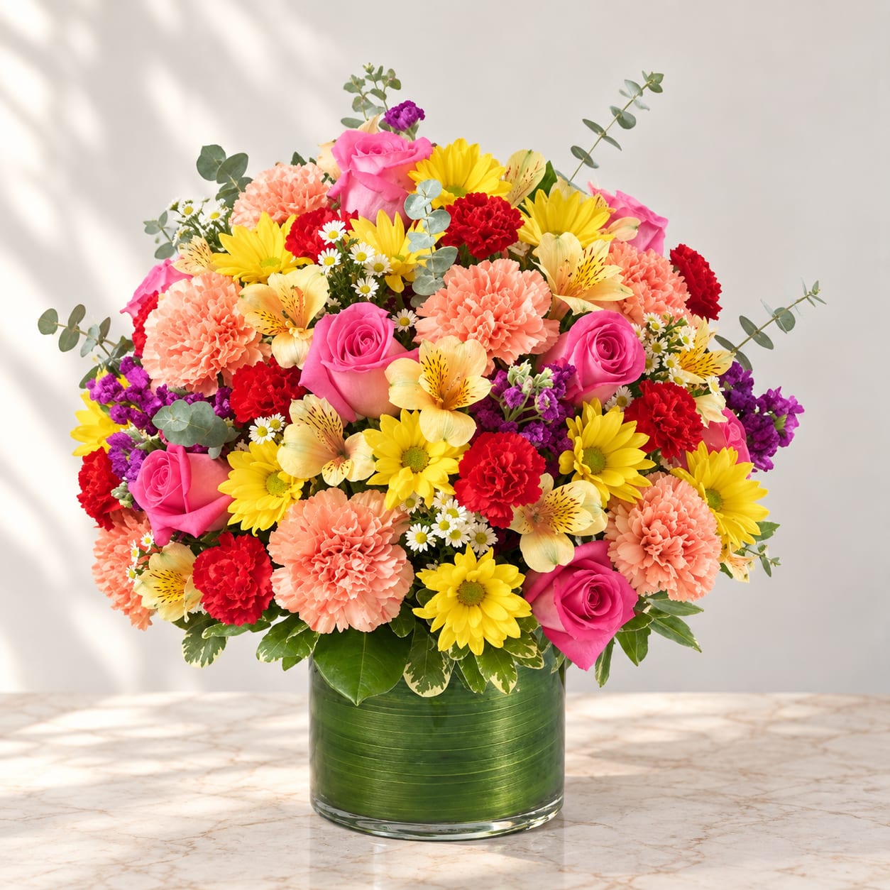 Colorful mixed bouquet in a green glass vase with pink, yellow, red, and peach flowers