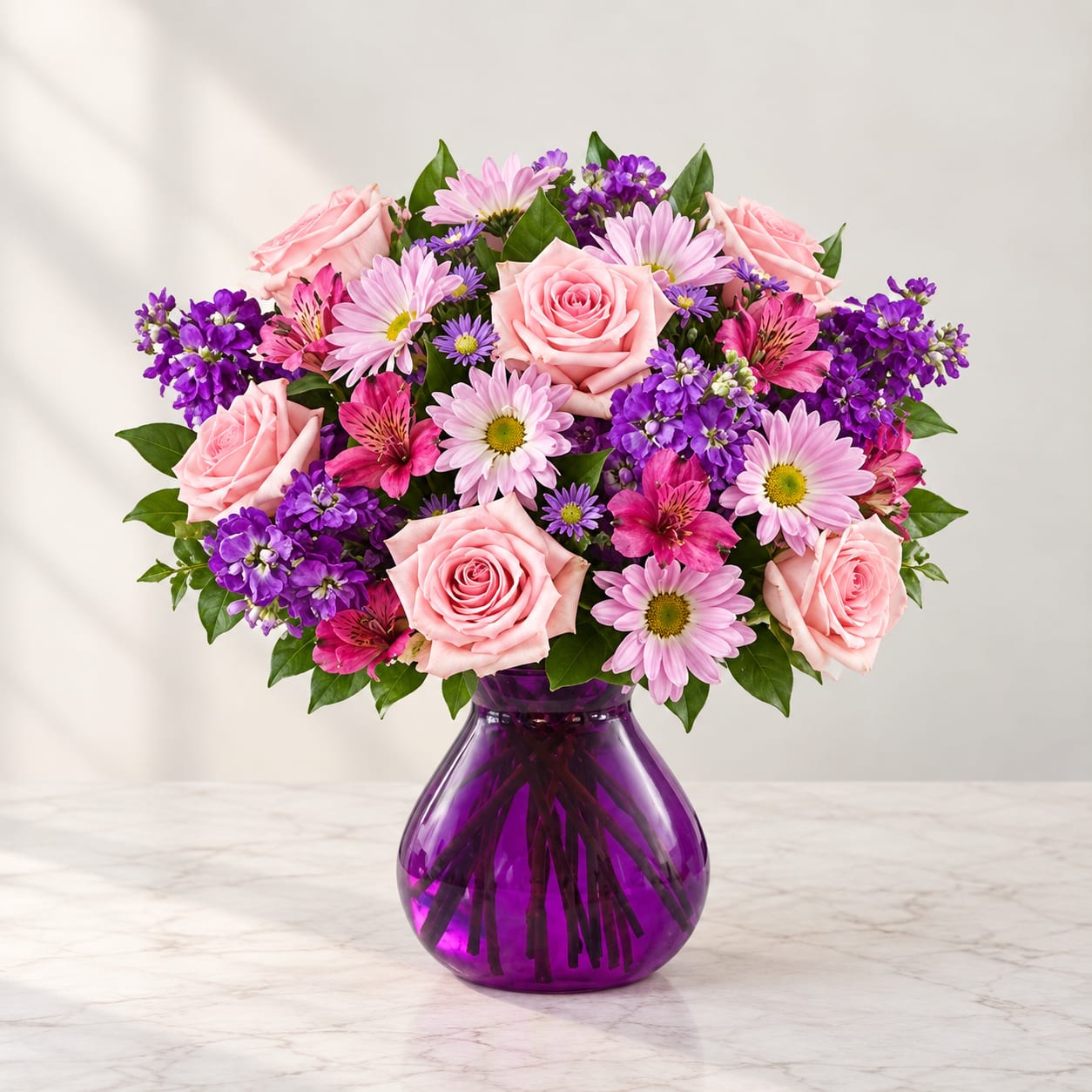 Pink roses and purple mixed flowers in a purple glass vase