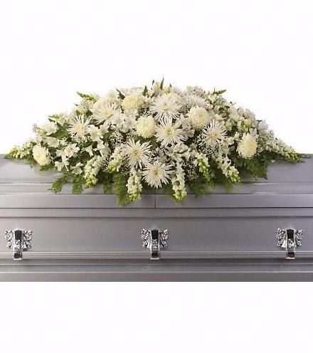 White floral casket spray with green accents on a gray casket