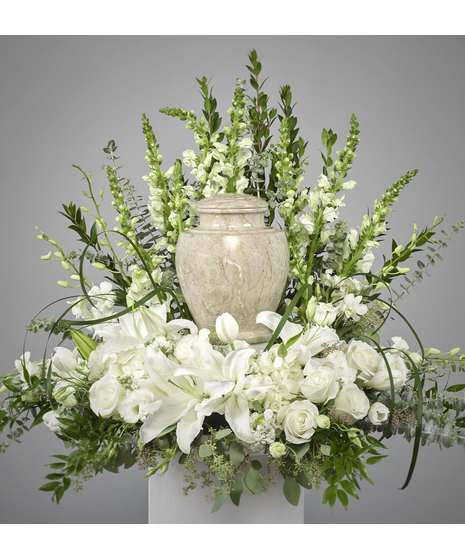 White floral arrangement with lilies and roses around a stone urn