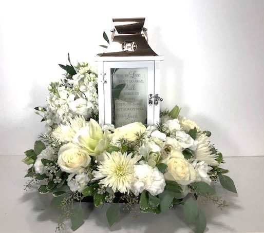 White floral arrangement around a white lantern with a candle inside