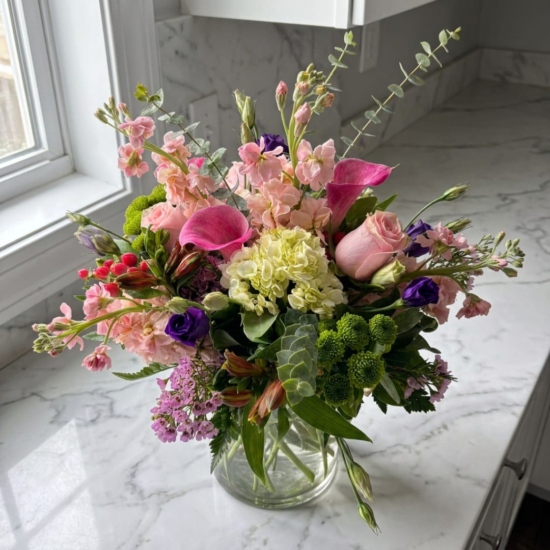 Mixed bouquet of pink, purple, and cream flowers in a clear glass vase