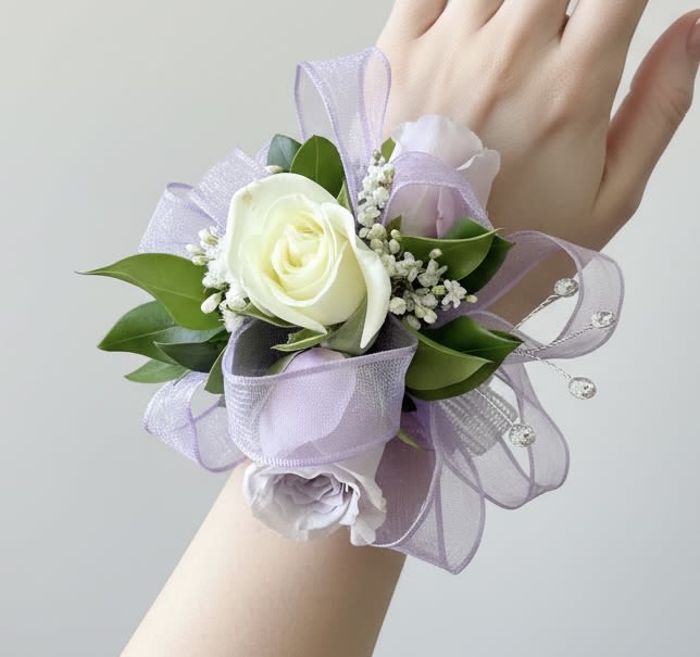 Lavender and white rose wrist corsage with ribbon and rhinestone accents on a person's hand.