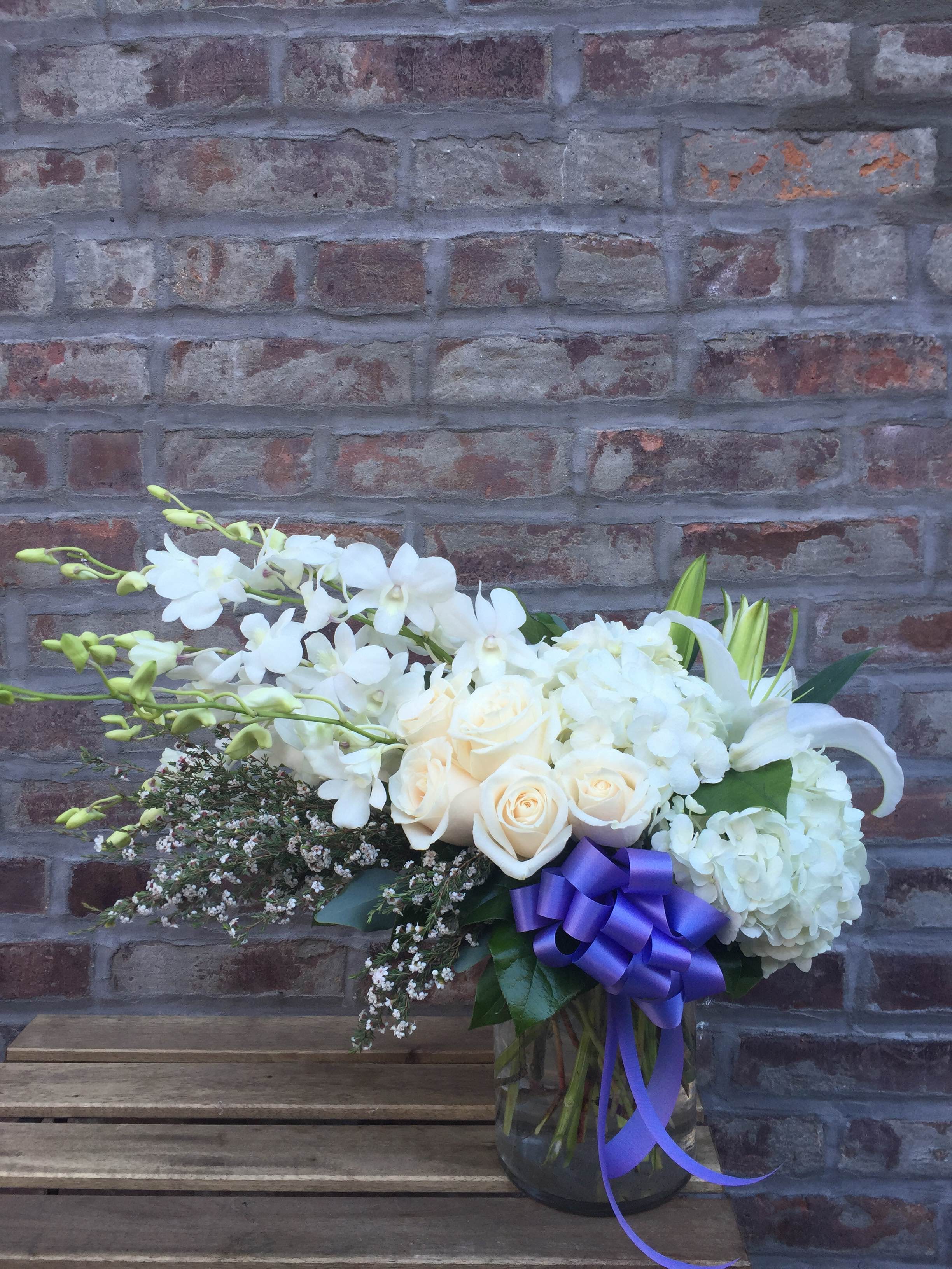 White floral arrangement in a glass vase with a purple ribbon