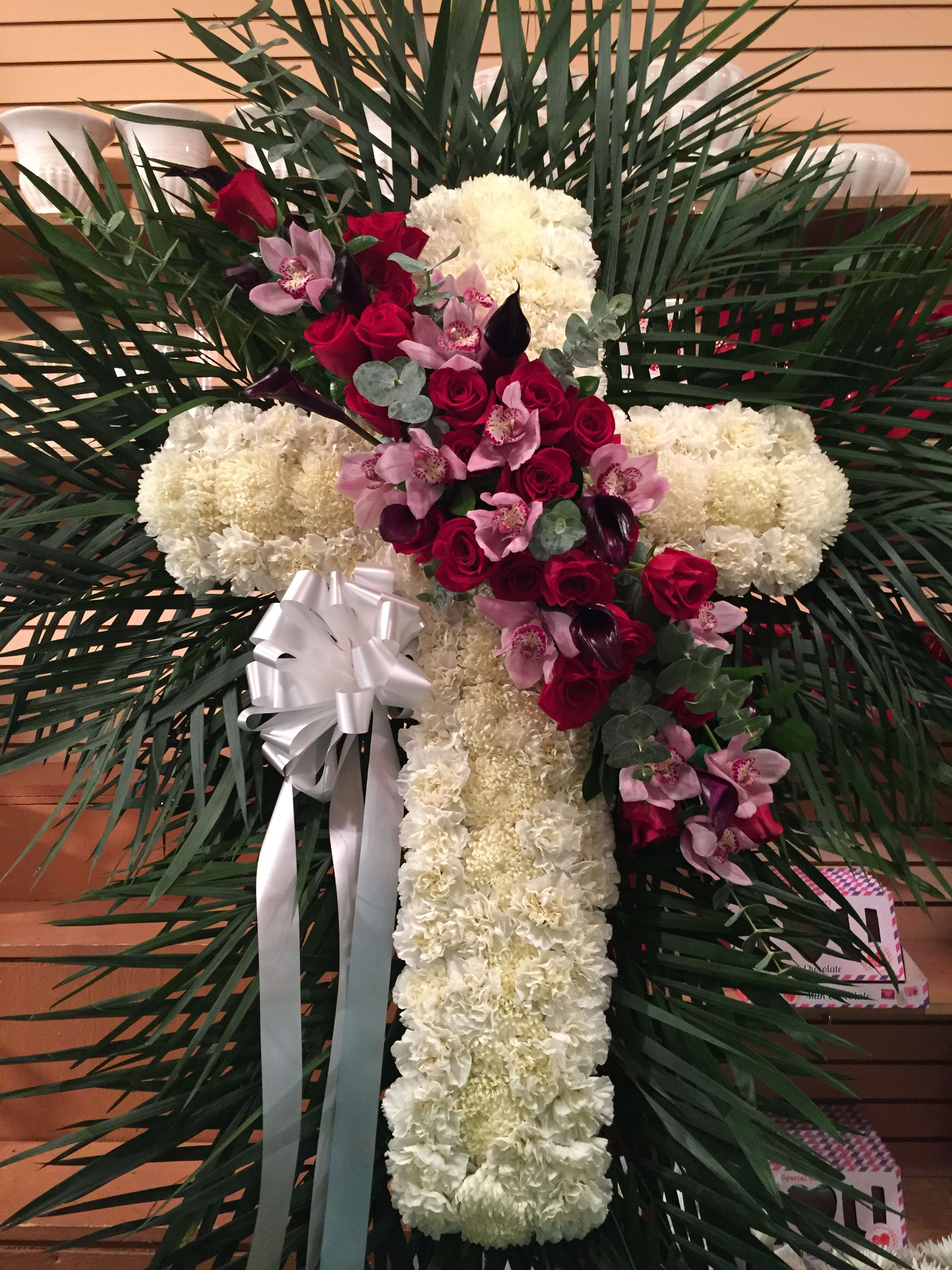 Cross-shaped floral tribute with white carnations, red roses, and pink orchids