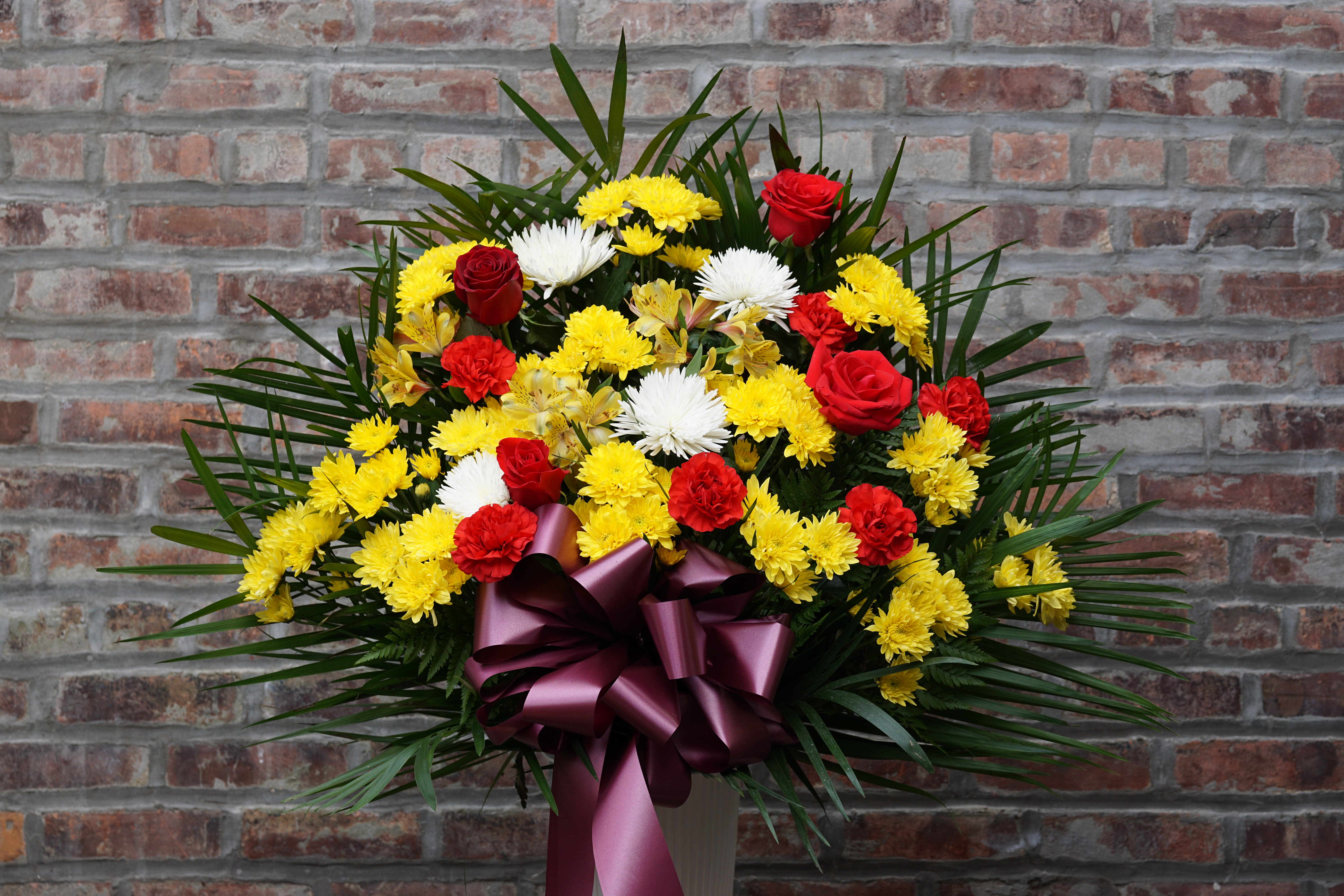 Standing floral spray with red, yellow, and white flowers and a purple ribbon