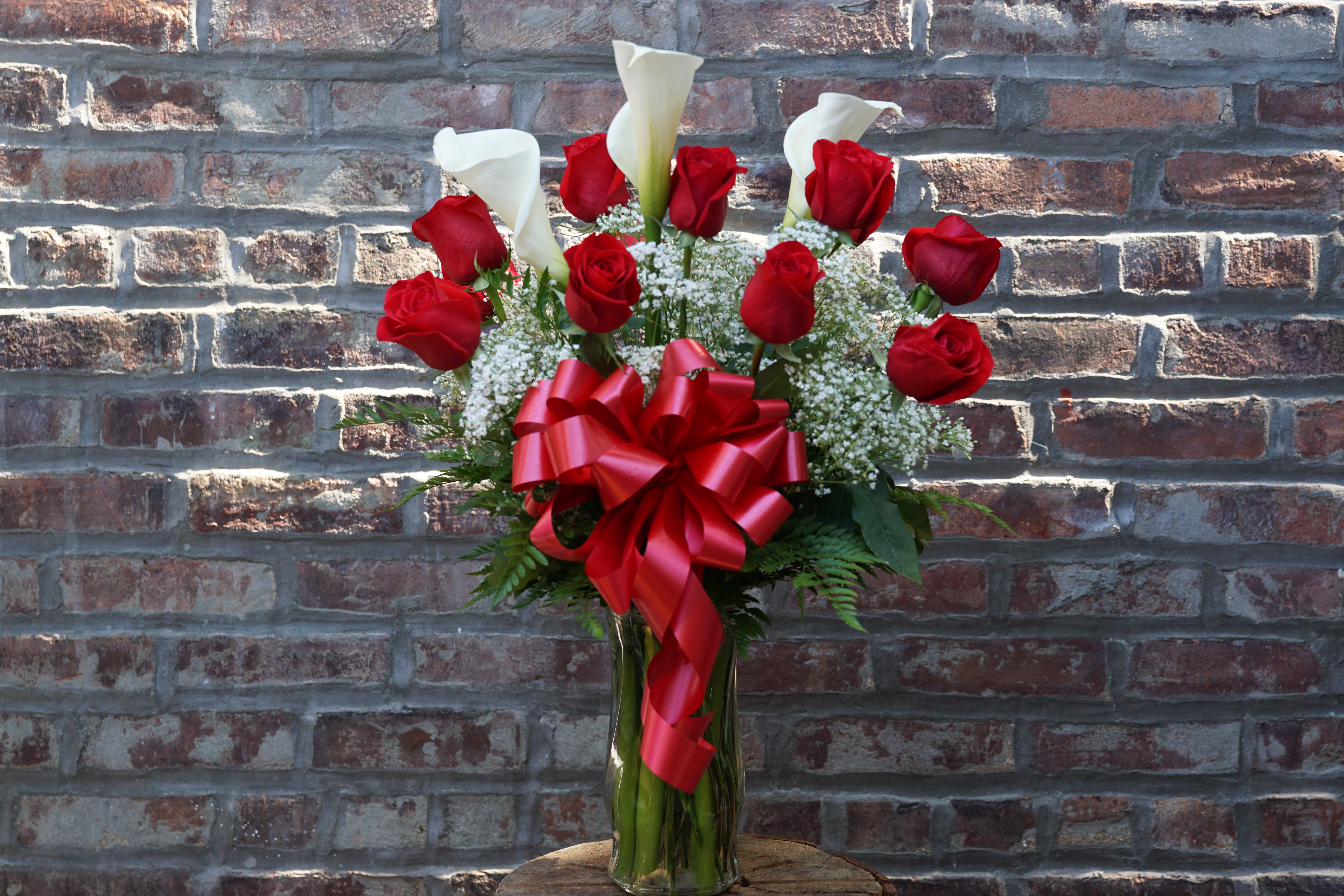 Red roses and white calla lilies in a glass vase with a red ribbon