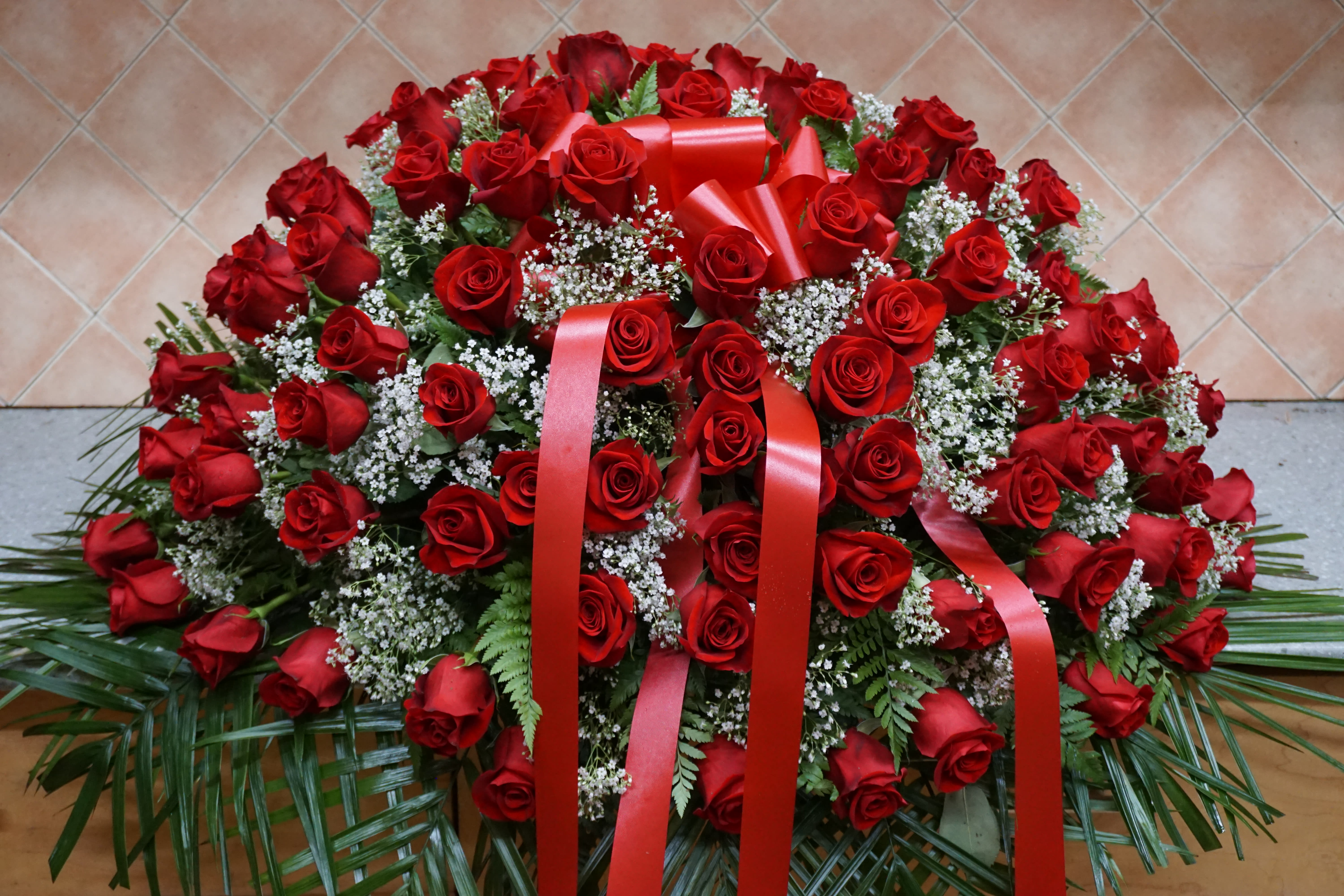 Large arrangement of red roses with white filler flowers and red ribbons