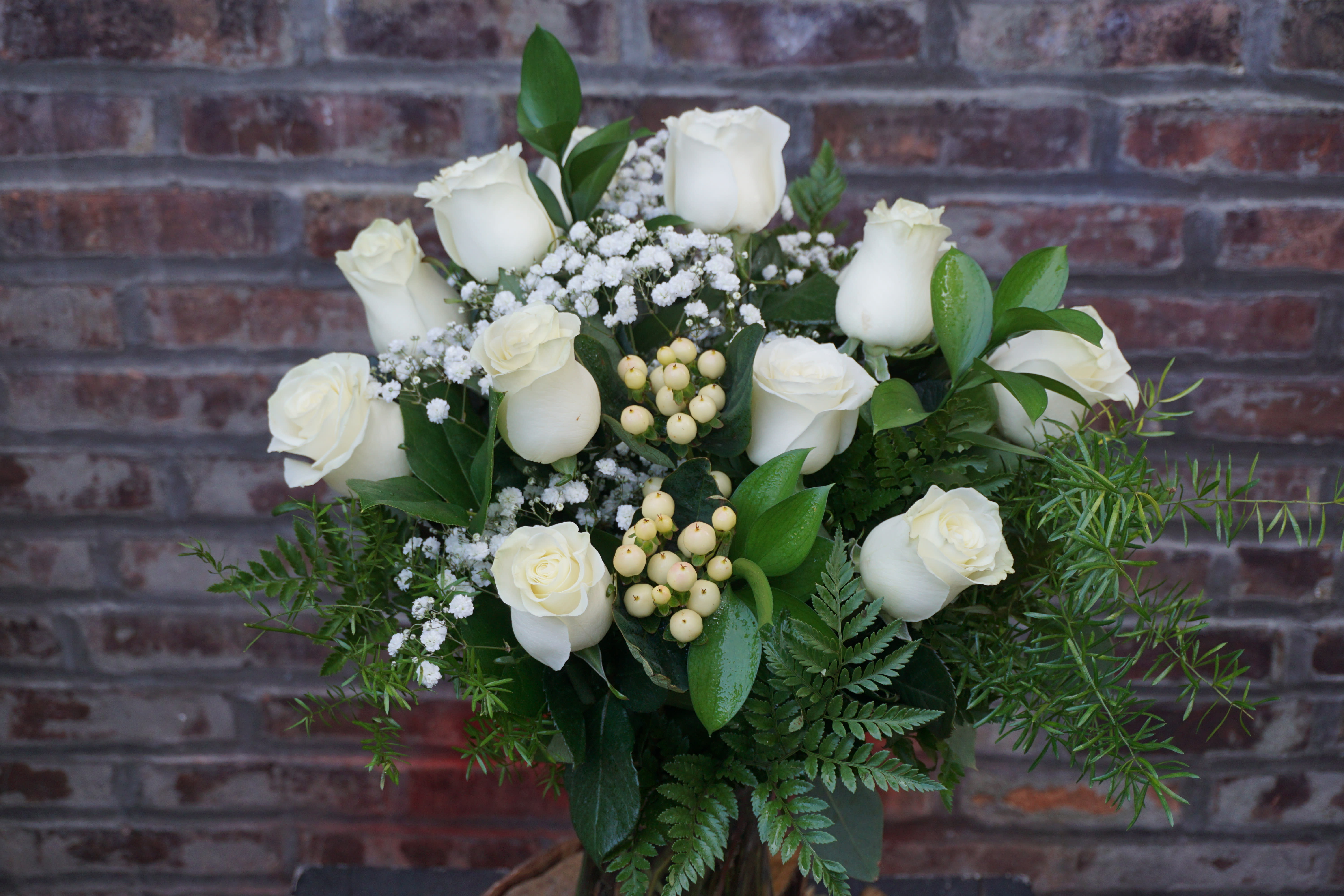 White roses arranged with baby's breath and greenery in a vase