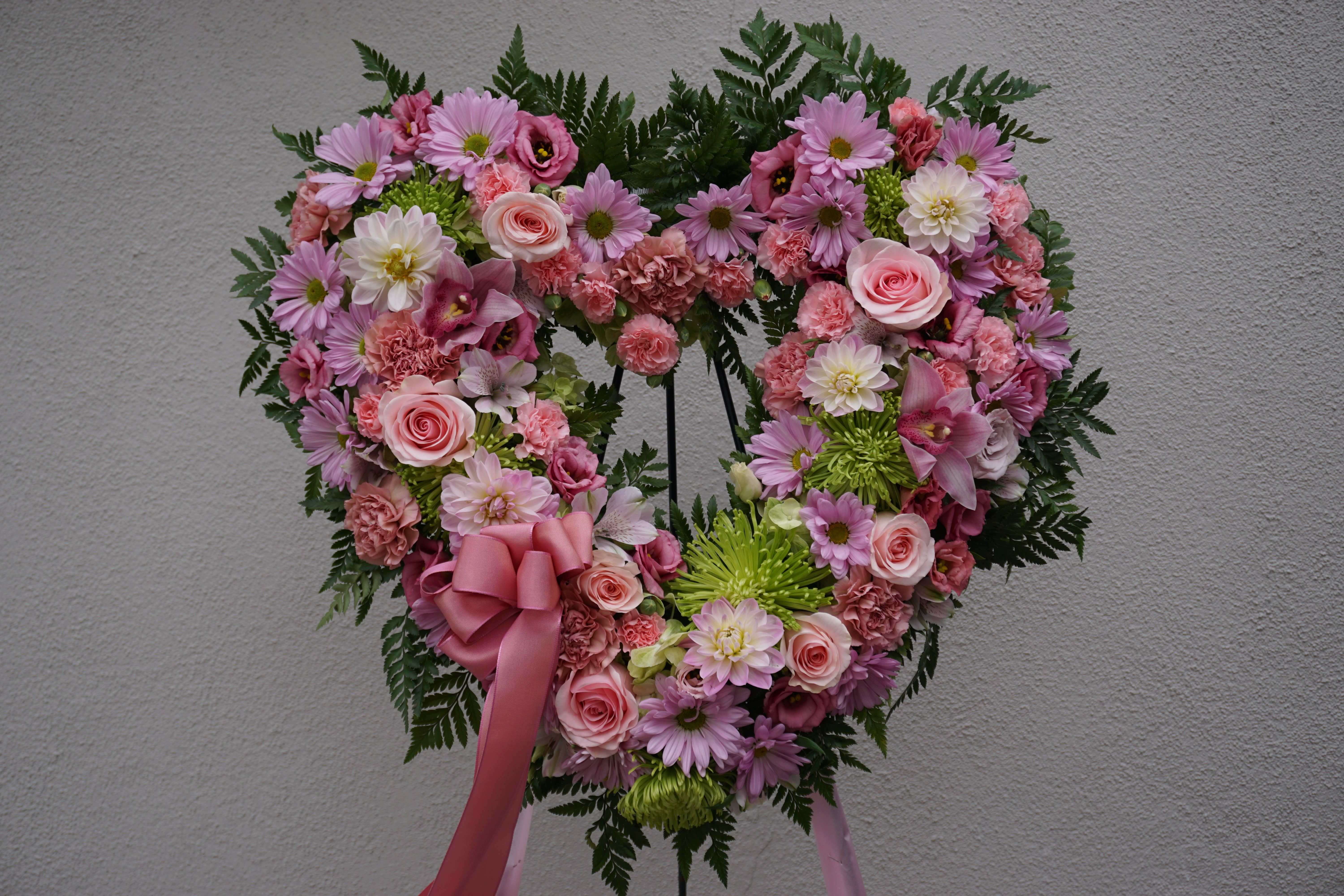 Heart-shaped floral wreath with pink and white flowers and a pink ribbon