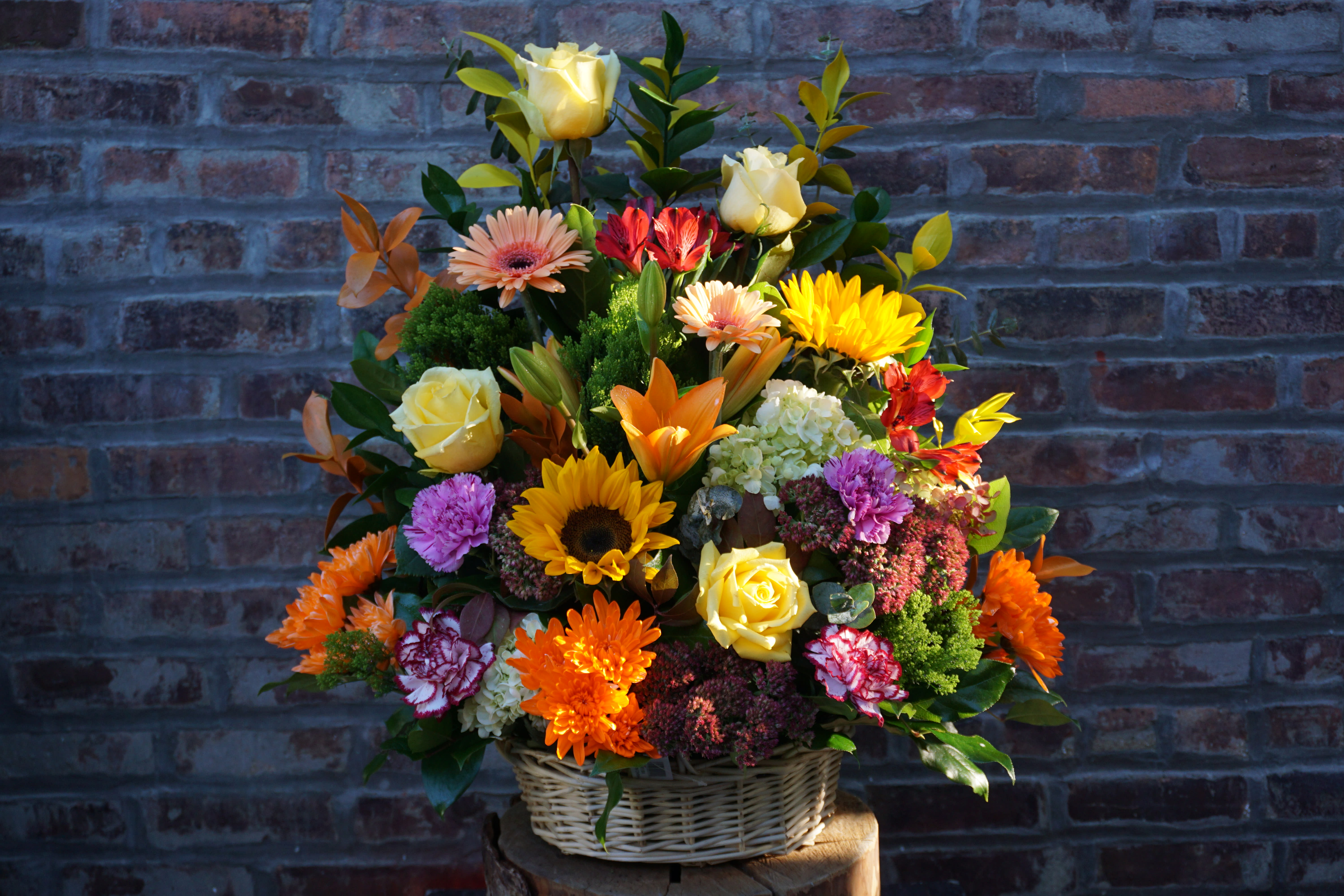 Mixed flower arrangement in a wicker basket with yellow roses and bright daisies