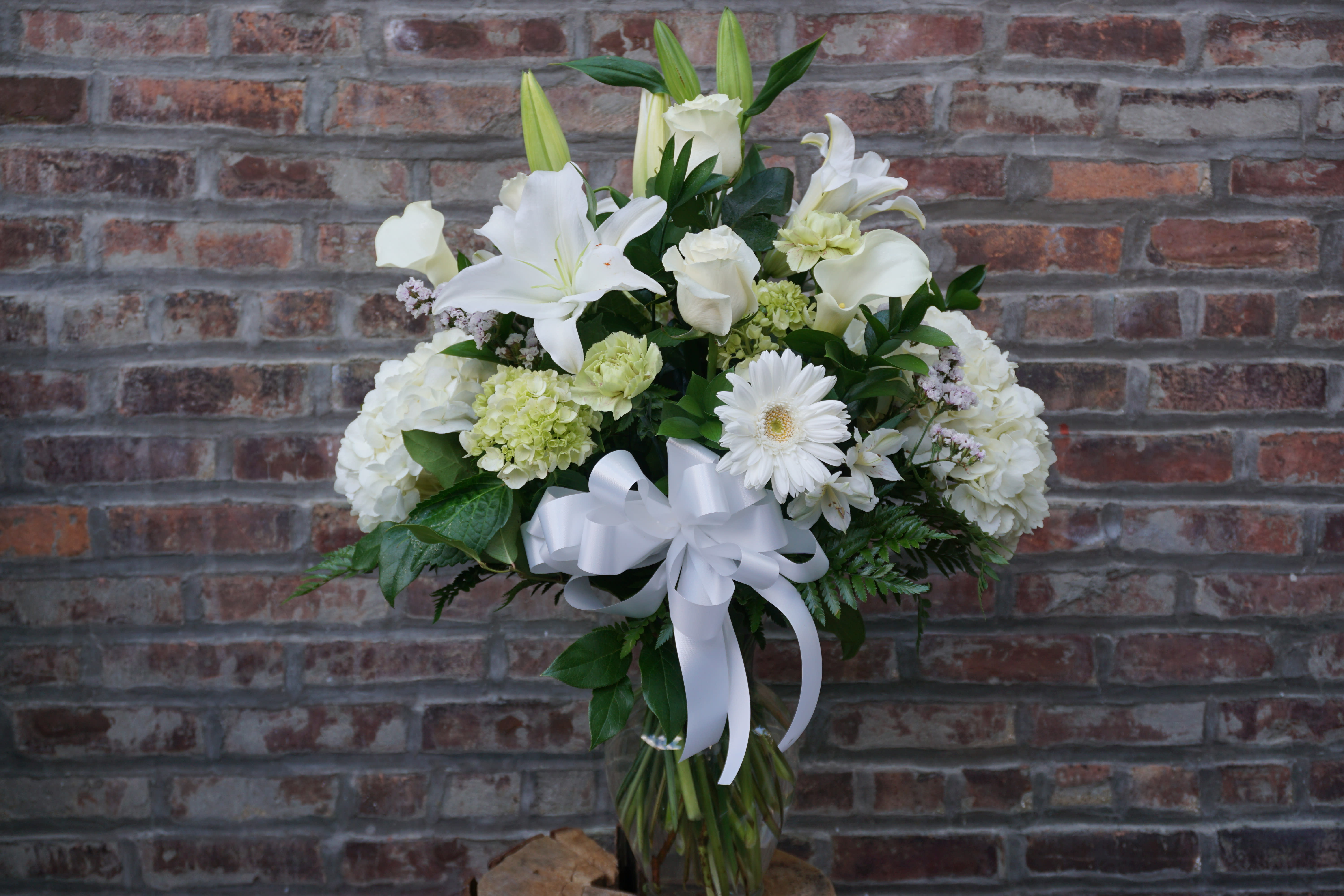 White floral arrangement with lilies, roses, and a ribbon bow