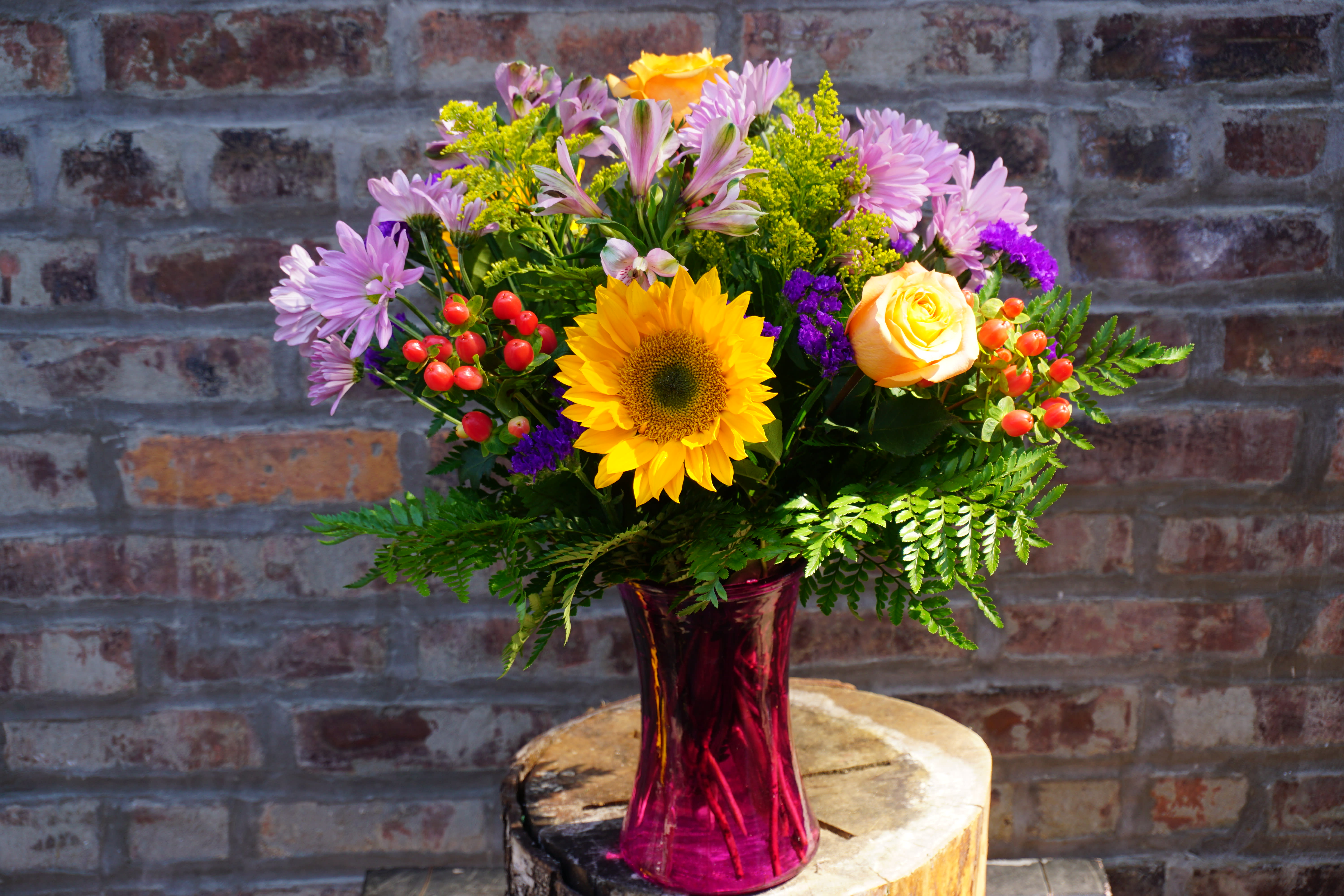 Mixed bouquet with a sunflower, roses, and purple daisies in a pink vase