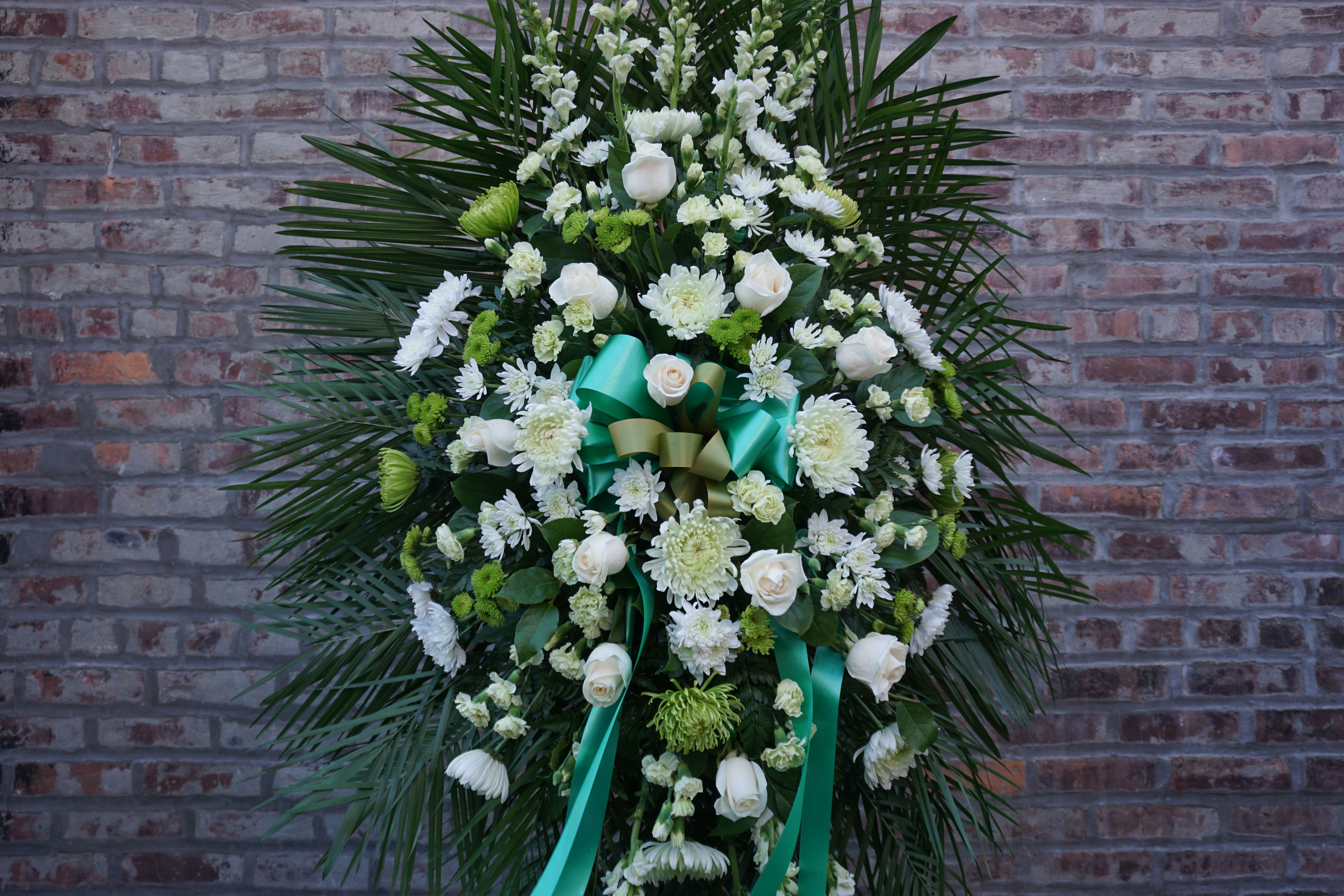 White floral standing spray with teal ribbons against a brick wall