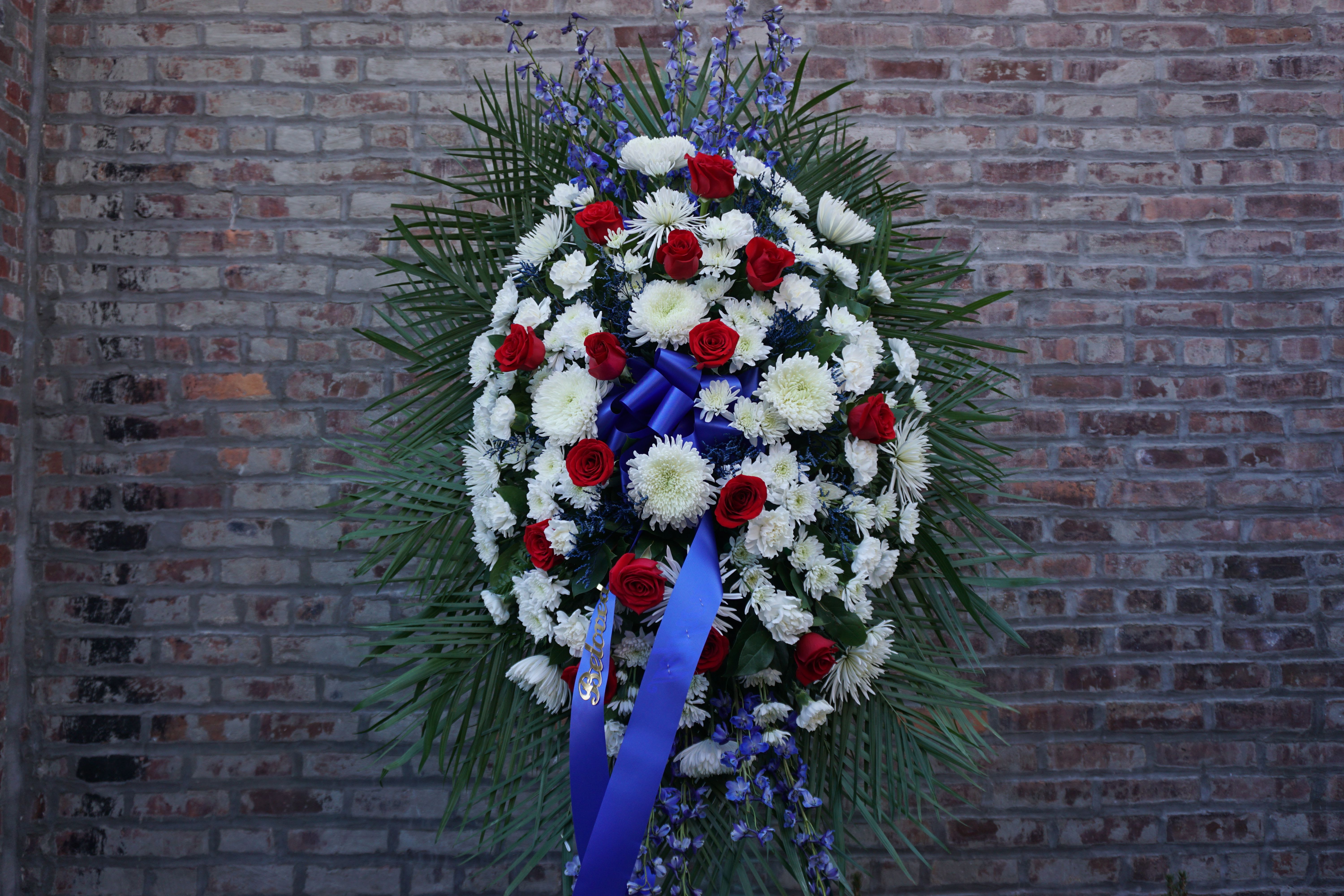 Standing funeral spray of red and white flowers with blue ribbon