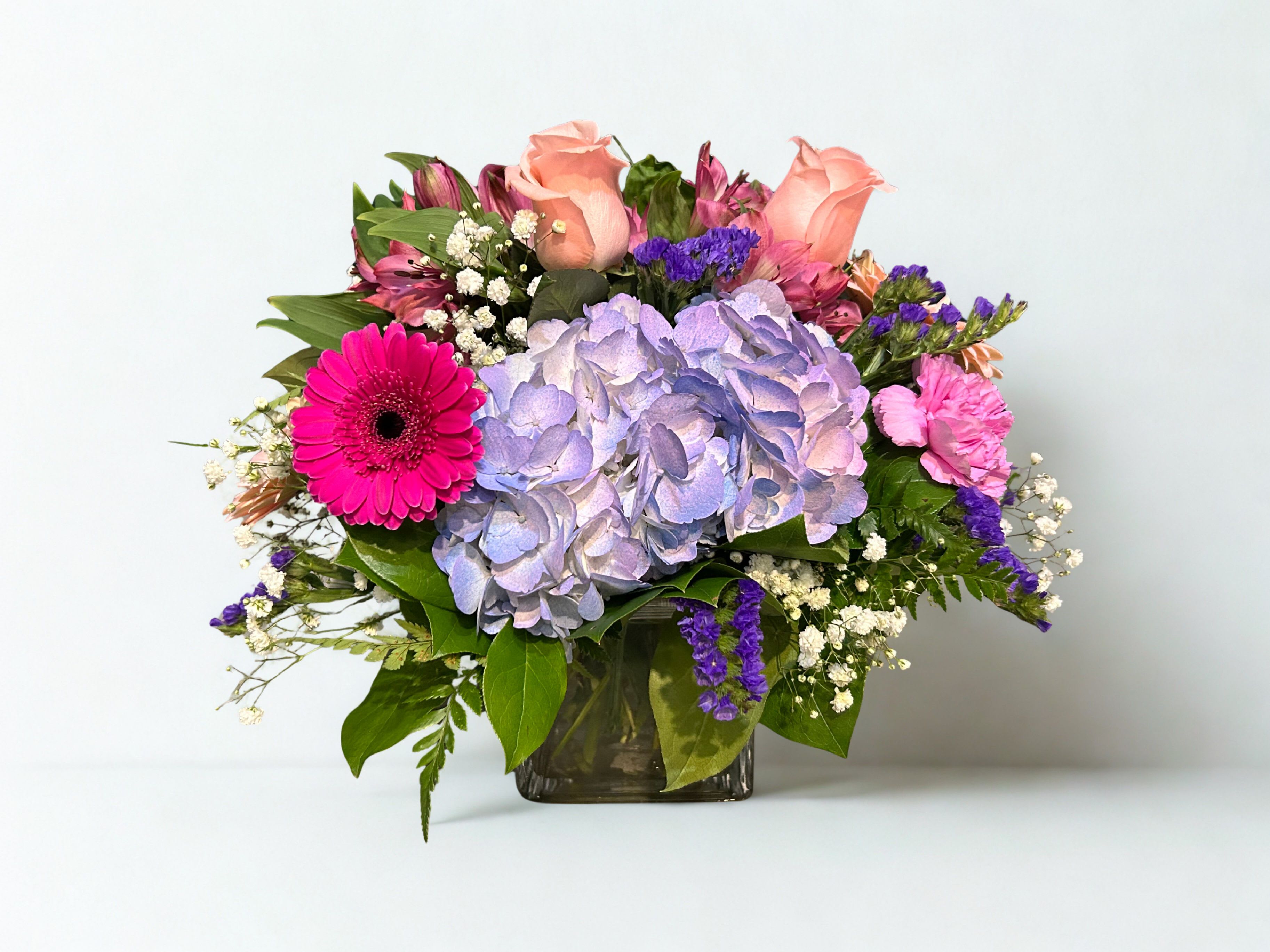 Mixed bouquet with hydrangea, roses, and gerbera daisies in a glass vase