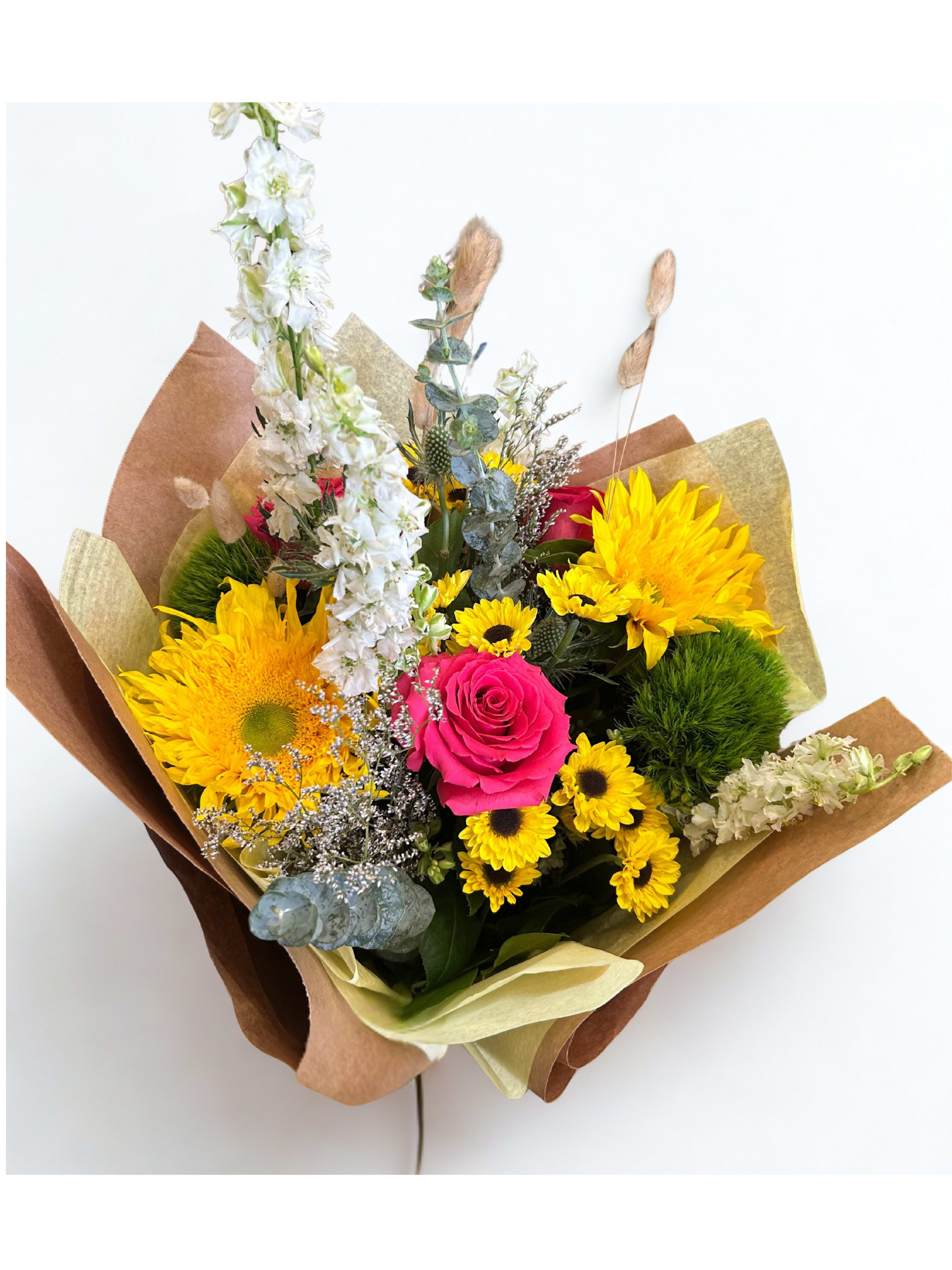 Bouquet with yellow sunflowers, a pink rose, and white flowers wrapped in brown paper