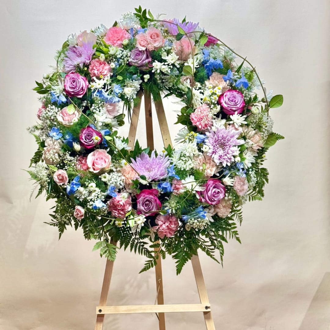 Circular floral wreath on a wooden easel with pink, purple, blue, and white flowers