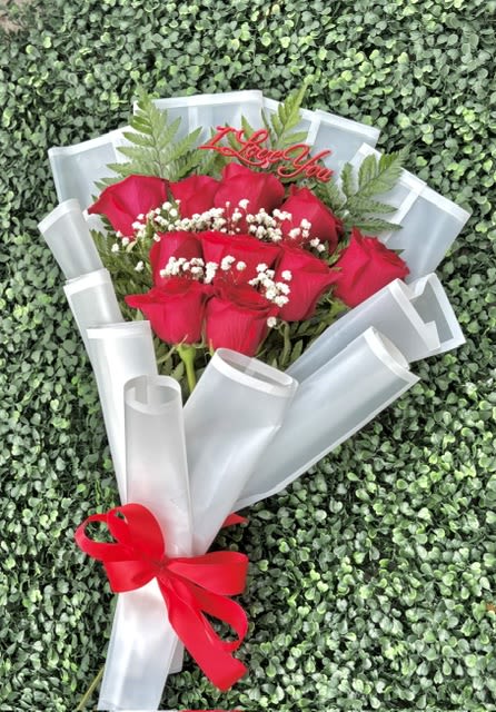 Red Rose Bouquet With White Fillers - Anniversary Bouquet - Vivid red roses take center stage in this Congrats Grad bouquet, making a bold, celebratory statement perfect for graduation gifts or an anniversary-style congratulation. The tight cluster of crimson blooms against crisp white accents and fern-like greenery creates a striking red-and-white contrast that reads both romantic and triumphant - the kind of bouquet that makes the person you're honoring feel truly seen and celebrated.  Carefully wrapped in layered white paper and finished with a bright red ribbon, the arrangement arrives gift-ready with a polished, photographed-worthy look. Small white filler flowers weave through the roses for texture, while the translucent white wrap keeps the focus on the blooms. A gold "Congrats Grad" topper and decorative gold accent add a festive, personal touch that signals the occasion at a glance.  Send this to a recent graduate, a proud parent, or anyone reaching a milestone to convey warmth, admiration, and excitement. Size and care: wrapped bouquet-handle gently, keep stems in fresh water and trim an inch before placing in a vase to extend vase life.
