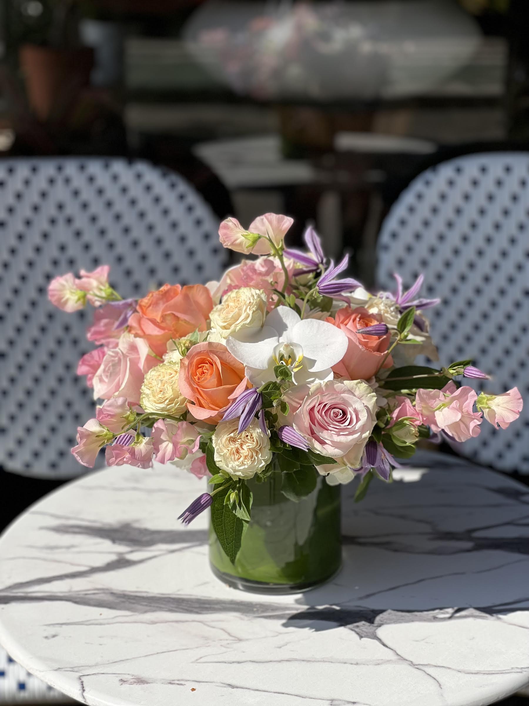 Pink and peach roses with white orchids in a glass vase