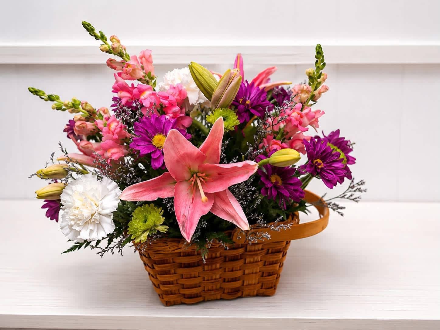 Basket arrangement with pink lilies, purple daisies, and white carnations