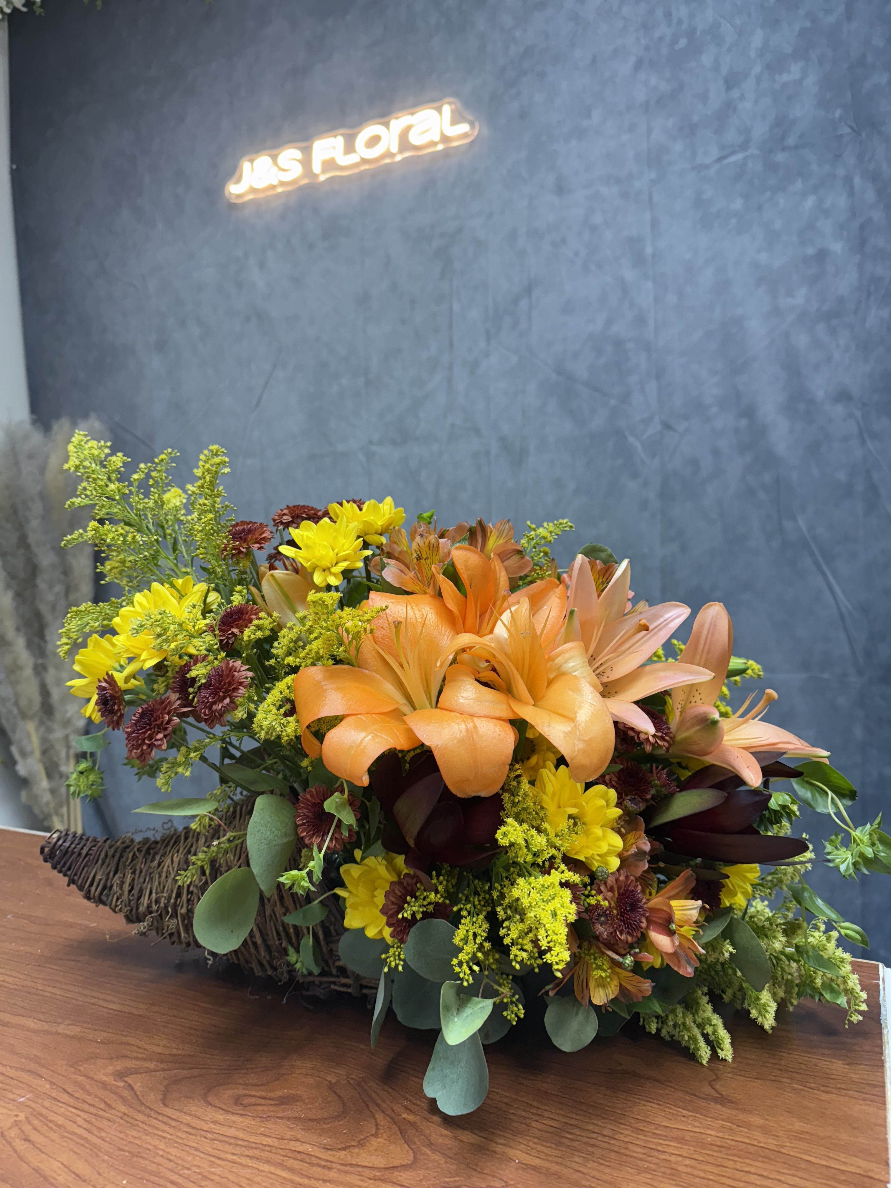 Cornucopia of Fall - Introducing our Cornucopia of Fall—a stunning arrangement featuring vibrant orange lilies, daisies and alstroemeria, celebrating the season’s natural beauty. This beautiful display brings together warmth, texture, and autumn charm in one perfect centerpiece.