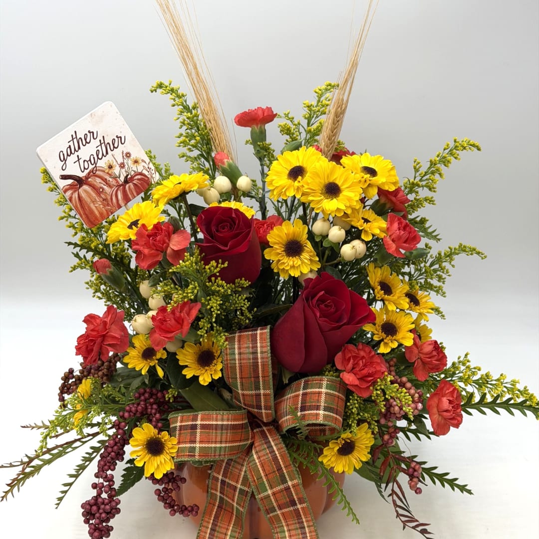 Fall floral arrangement with red roses, yellow daisies, and a plaid bow in a pumpkin container