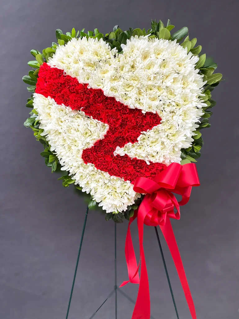 Heart-shaped floral wreath with red ribbon on a stand