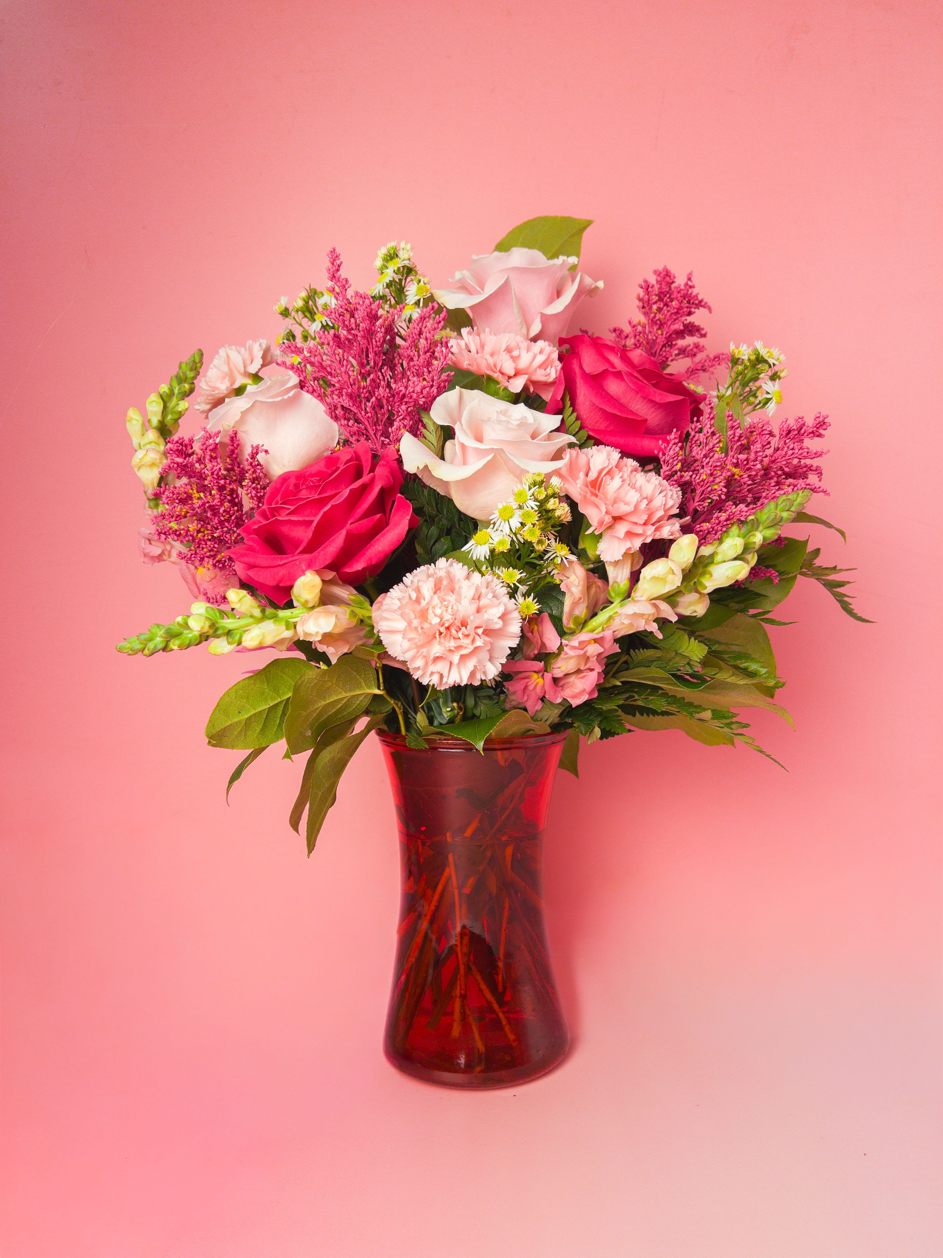 Blush Theory Arrangement - A cheerful contrast of hot pink and pastel blooms, flawlessly styled in a glass vase. This everyday arrangement makes a bold and soft statement while instantly brightening the day. Perfect as a birthday surprise, anniversary gift, or a simple thinking-of-you gesture. The pink palette and fresh green foliage creates an immediate sense of joyful warmth; the person you're gifting will feel seen and celebrated the moment this arrangement arrives.  This mixed arrangement emphasizes color and texture over strict flower types, so while roses, carnations, snapdragons, and daisy-like accents are often used, seasonal substitutions preserve the hot pink and soft blush look. The arrangement ships ready to display and fits nicely on dining or bedside tables.  A perfect pick from your Baltimore florist for local gifting, this design is ideal for an array of occasions. Our florist team hand-designs each arrangement, sources seasonal blooms to keep the color story consistent, and includes delivery notes to help your gift arrive exactly as intended.