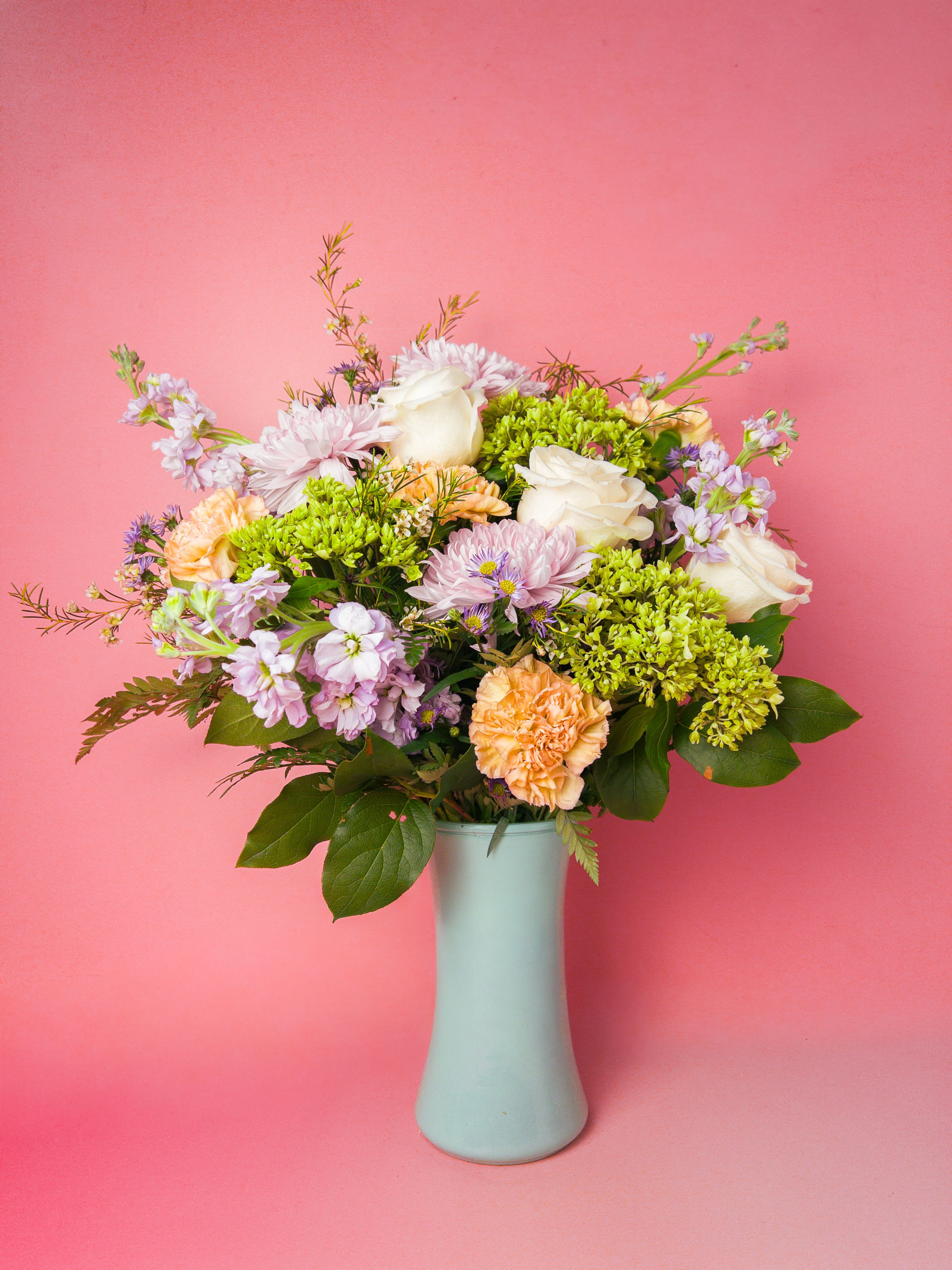 Garden Muse Arrangement - A soft, garden-fresh bouquet in peaches, creams, lavenders and bright spring green. This flower arrangement reads like a sunny stroll through a cottage garden. As a birthday bouquet, or cheerful thank-you, its airy, rounded silhouette and gentle pastels make the person you're thinking of feel seen and celebrated.   The arrangements composition focuses on the soft color story-blush and cream roses, peach blooms, pale lavender accents and lively green clusters layered for texture and movement-so the garden vibe stays consistent even when seasonal substitutions are needed. The vase offers a clean, modern base that complements the arrangement's whimsical branching stems and garden-style feel. Order with confidence from The Flower Cart for reliable Flower Delivery in Baltimore; our florist team thoughtfully prepares each arrangement to arrive fresh and ready to brighten their day.