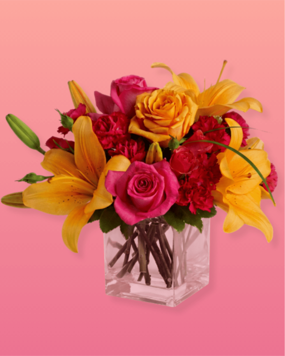 Pink and yellow flower arrangement in a clear square vase
