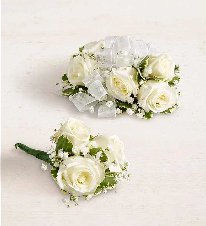 Two white rose boutonnieres with ribbon accents on a light background
