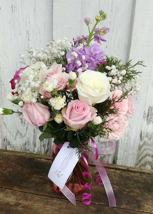 Pink and white rose bouquet in a glass vase with purple flowers