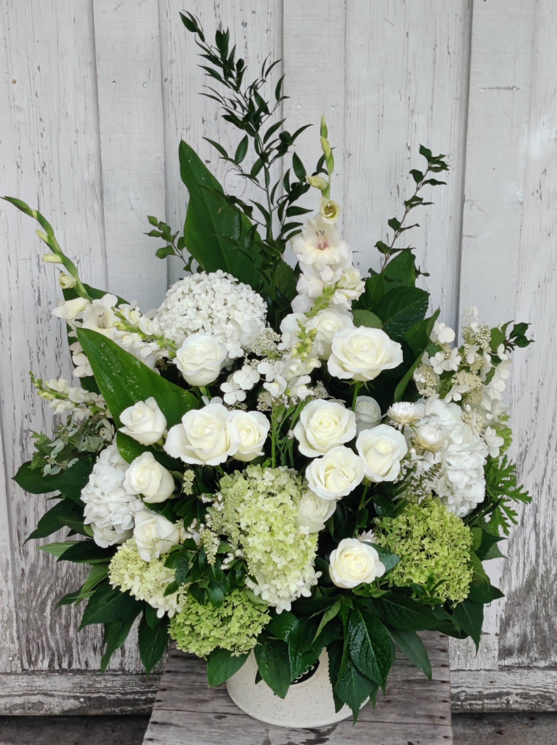 White roses and hydrangeas arranged in a white vase with tall greenery