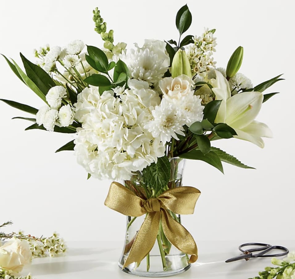 White floral bouquet in a clear glass vase with a gold ribbon