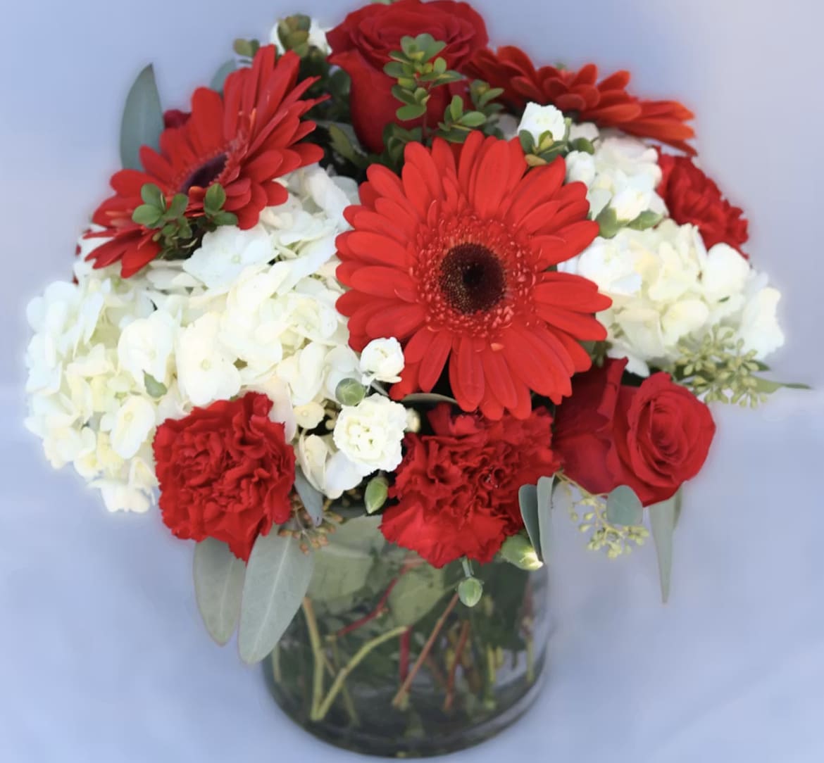 Red gerbera daisies, roses, and white hydrangeas in a glass vase