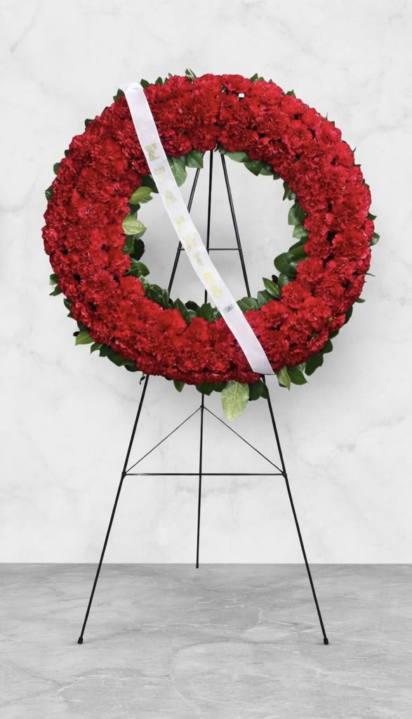 Red floral wreath on a black stand with a white ribbon